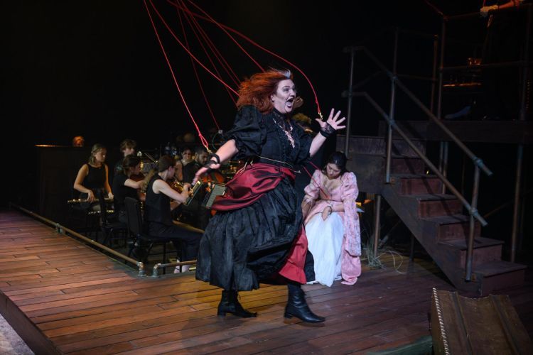 Opera singer in black gown with a silk red sash and red string coming from her hands and body as if being controlled like a puppet